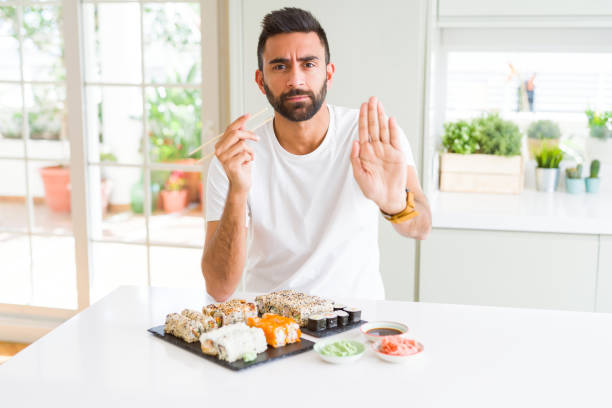 istock Handsome hispanic man eating asian sushi using chopsticks with open hand doing stop sign with serious and confident expression, defense gesture 1167774932
