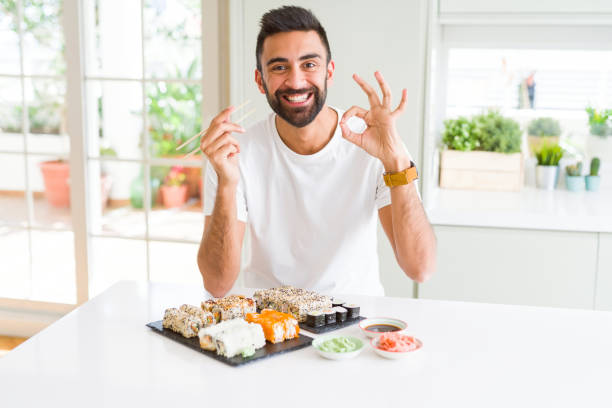 istock Handsome hispanic man eating asian sushi using chopsticks doing ok sign with fingers, excellent symbol 1167774933