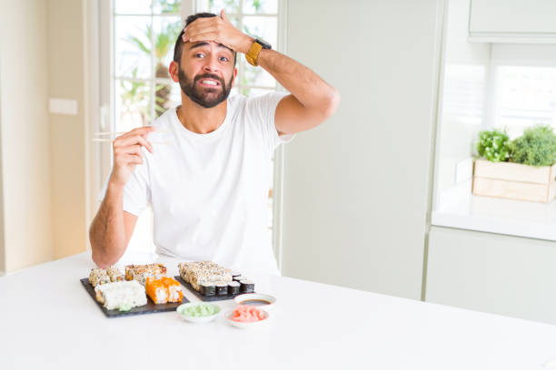istock Handsome hispanic man eating asian sushi using chopsticks stressed with hand on head, shocked with shame and surprise face, angry and frustrated. Fear and upset for mistake. 1167774934