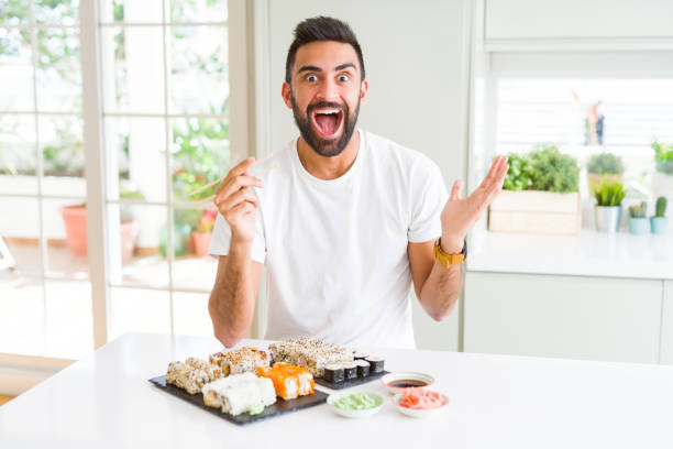 istock Handsome hispanic man eating asian sushi using chopsticks very happy and excited, winner expression celebrating victory screaming with big smile and raised hands 1167774935