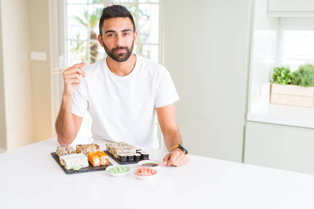 istock Handsome hispanic man eating asian sushi using chopsticks with a confident expression on smart face thinking serious 1167774943