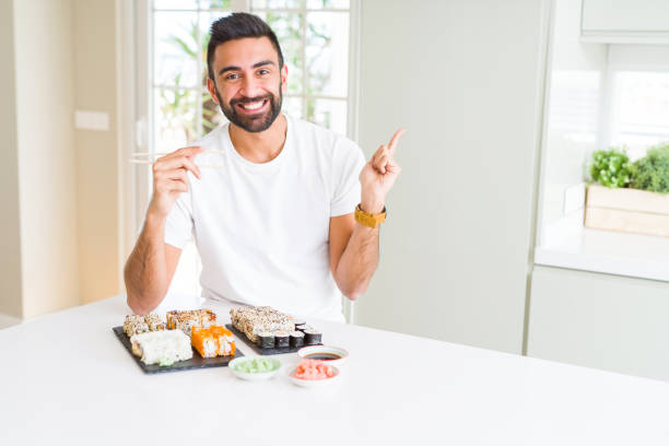 istock Handsome hispanic man eating asian sushi using chopsticks very happy pointing with hand and finger to the side 1167774949