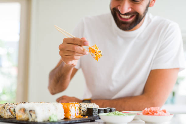 homem considerável que sorri feliz que aprecia comer o sushi asiático colorido fresco usando chopsticks - asian cuisine horizontal spice restaurant - fotografias e filmes do acervo