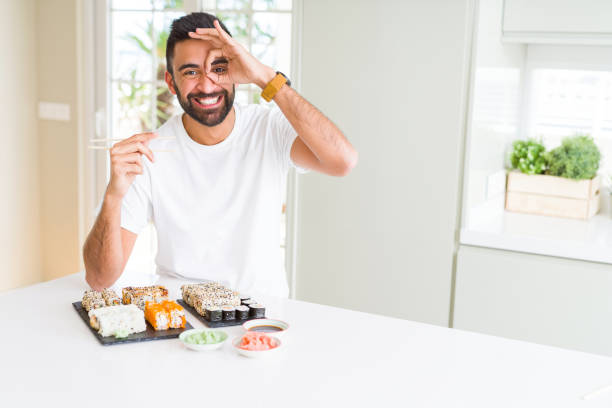 istock Handsome hispanic man eating asian sushi using chopsticks with happy face smiling doing ok sign with hand on eye looking through fingers 1167775076