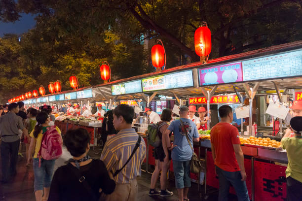 Donghuamen Night Market snack street near Wangfujing in Beijing Beijing, China - July 27, 2013: Chinese foods (mostly snacks) and drinks are prepared and sold by market vendor at the Donghuamen Night Market - the most popular snack street in Beijing - located at the northern entrance of Wangfujing Street. The vendors are preparing and selling deep fried meat and seafood - including some exotic foods such as silkworm and snakes - served on a stick, but also more ordinary foods like bread, dumplings, noodles, fruit, vegetables and soft drinks. The image was captured at night in low light at high ISO. wangfujing stock pictures, royalty-free photos & images