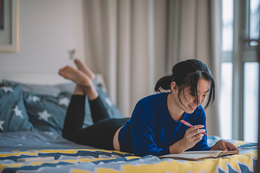 an asian chinese female teenager lying on bed having fun writing and studying