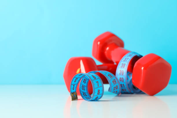 istock Dumbbells and measuring tape on white table against blue background 1167777820