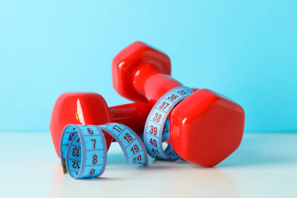 istock Dumbbells and measuring tape on white table against blue background 1167778486