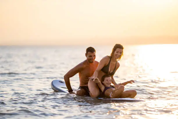 family mother father and daughter having fun with surfboard paddle board on lake in summer sunset evening series