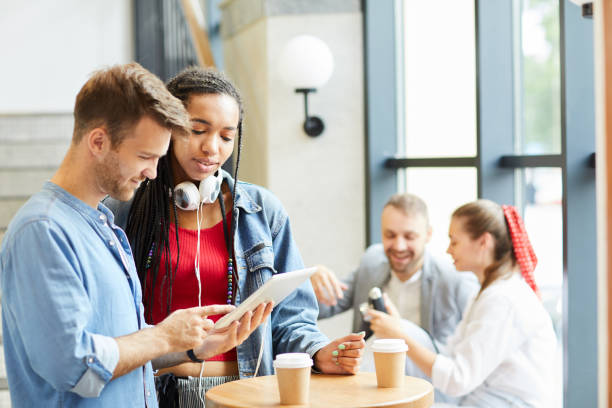 istock Young guy with stubble standing at round table in coffee shop and showing interesting internet resource to friend 1167782343