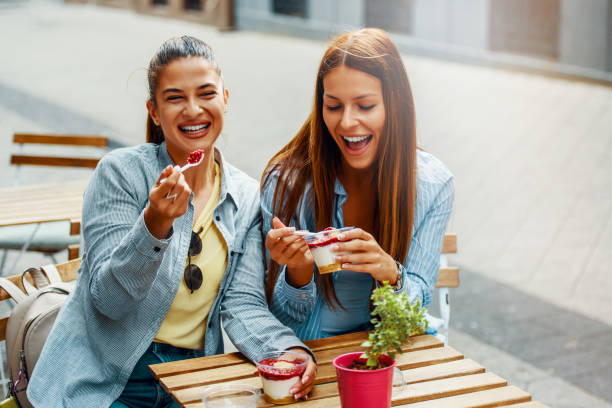 Two female friends having fun eating cheesecake outdoors stock photo
