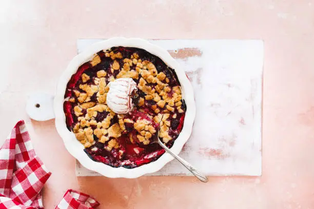 Summer berry crumble. Vegan crumble in a baking dish with serving spoon on summer table. Top view, blank space