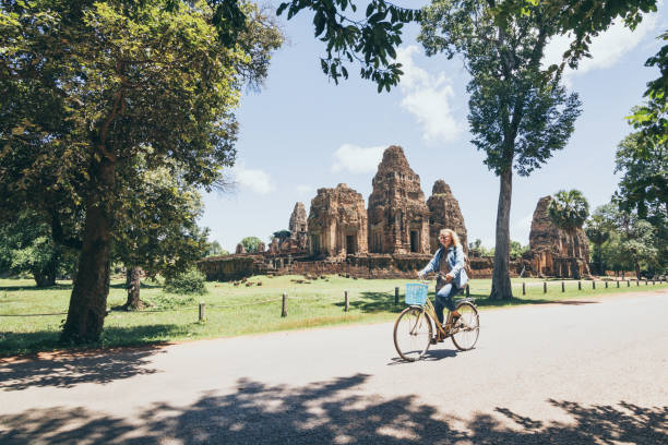 Young woman riding bicycle next to Pre Rup temple in Angkor Wat complex, Cambodia stock photo
