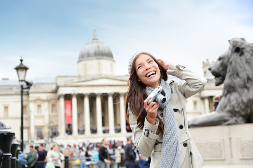 London tourist woman on Trafalgar Square taking photo holding camera smiling happy laughing having fun. Beautiful multiracial Asian Caucasian girl on travel vacation in London, England, United Kingdom