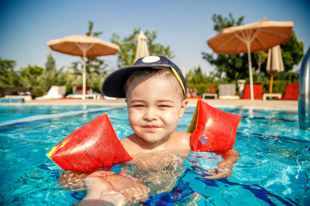 ein kleiner junge lernt im sommer mit unterstützung der hände seines vaters im pool schwimmen - early teens child swimming pool swimming stock-fotos und bilder