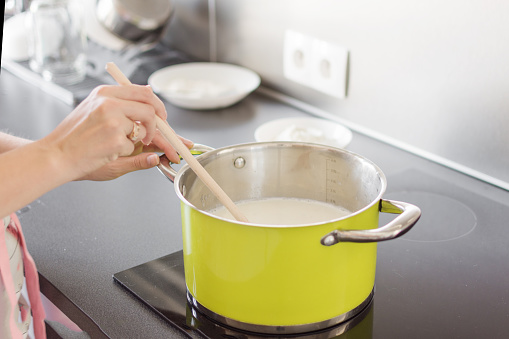 Woman hand is mixing boiling milk with wooden spoon.