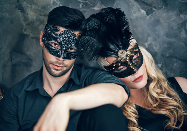 bella coppia in misteriosa maschera nera seduta sul pavimento in studio - women gothic style sensuality mystery foto e immagini stock