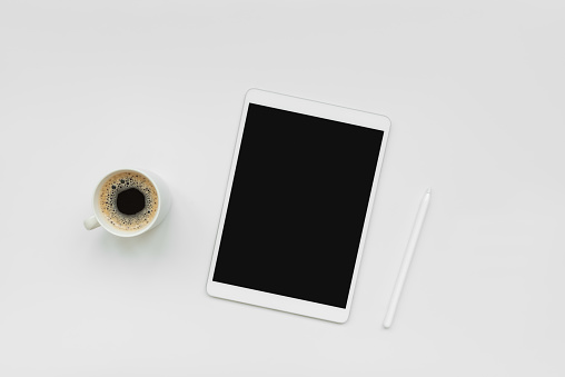 Tablet, pencil and cup of coffee on white desk. Top view. Copy space. Mock-up