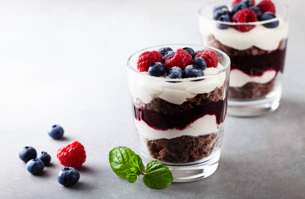Layered trifle dessert with chocolate sponge cake, whipped cream, berries and fruit jelly in serving glasses. Layered trifle dessert with chocolate sponge cake, whipped cream, berries and fruit jelly in serving glasses with copy space. cake jar stock pictures, royalty-free photos & images