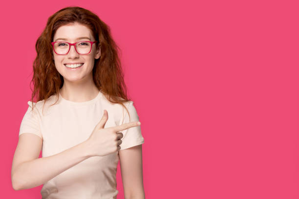istock Redhead woman in glasses looking at camera pointing finger aside 1167799918