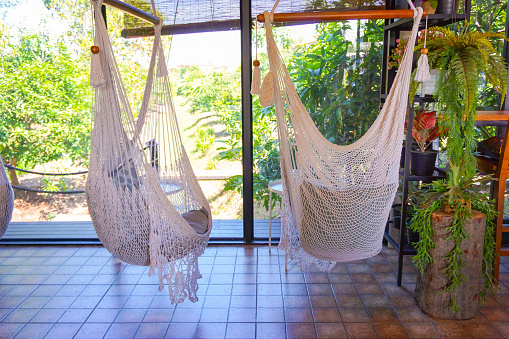 Empty white knitting rope swings hanging by the window in cafe, white hammock.