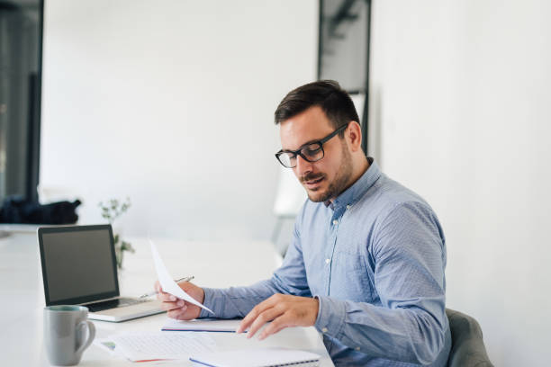 istock Happy young businessman looking at papers graphs and charts using laptop at his office desk 1167802897