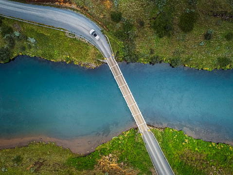 Aerial shot of a bridge over a blue coloured river in beautiful nature in Iceland. Blue clear water is running under the bridge. White car is driving over the bridge.