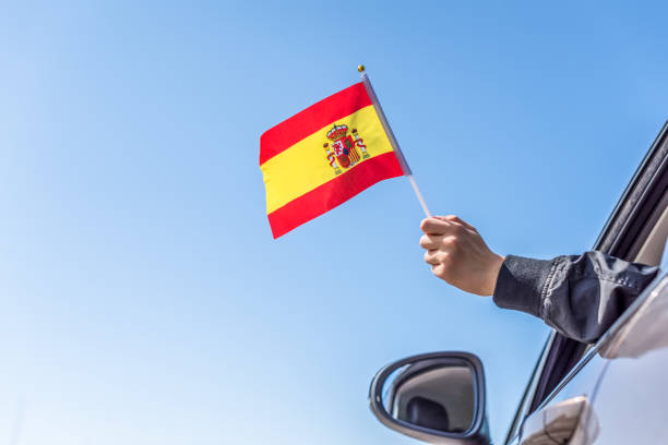 istock Boy holding Spanish Flag from the open car window on the sky background. Concept. 1167805522