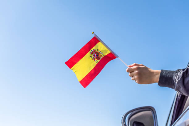 istock Boy holding Spanish Flag from the open car window on the sky background. Concept. 1167805525