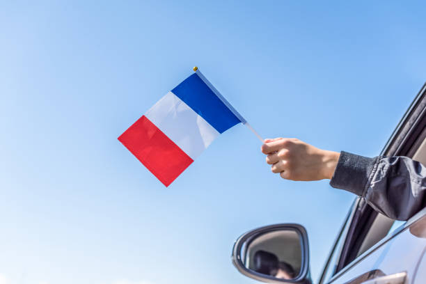Boy holding France Flag from the open car window on the sky background. Concept. stock photo