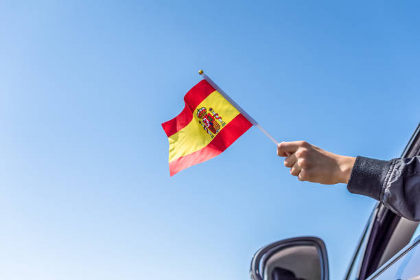 istock Boy holding Spanish Flag from the open car window on the sky background. Concept. 1167805564