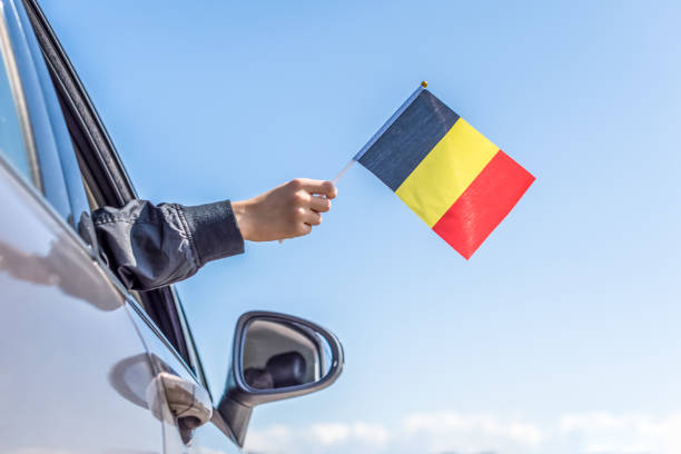 istock Boy holding Belgian Flag from the open car window on the sky background. Concept 1167806154