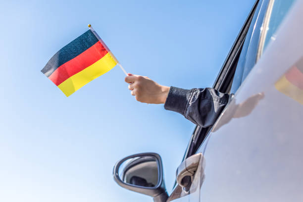istock Boy holding Germany Flag from the open car window on the sky background. Concept. 1167806174