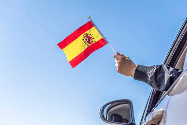 istock Boy holding Spanish Flag from the open car window on the sky background. Concept. 1167806226