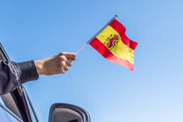 istock Boy holding Spanish Flag from the open car window on the sky background. Concept. 1167806229