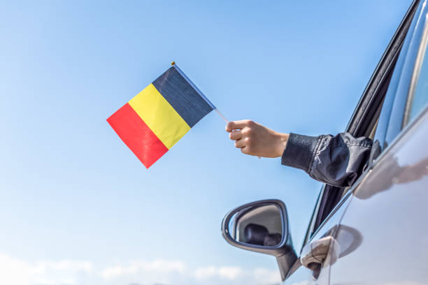 istock Boy holding Belgian Flag from the open car window on the sky background. Concept 1167806276