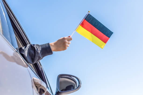 istock Boy holding Germany Flag from the open car window on the sky background. Concept. 1167806279