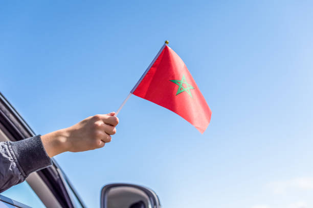 istock Boy holding Morocco Flag from the open car window on the sky background. Concept 1167807489
