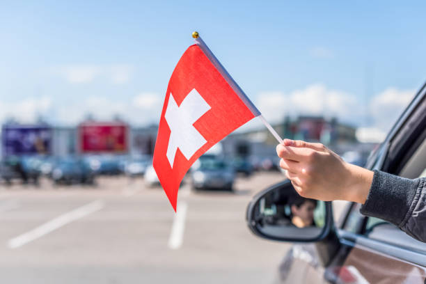 Boy holding Swiss Flag from the open car window on the parking of the shopping mall. Concept. Switzerland Boy holding Swiss Flag from the open car window on the parking of the shopping mall. Concept.  Switzerland schengen agreement photos stock pictures, royalty-free photos & images