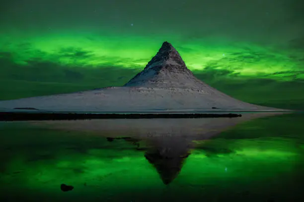 The famous mount kirkjufell un western iceland on a clear night with aurora borealis. The mountain mirror in the water.