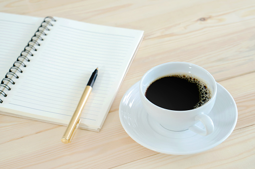 Notebook pen and cup of coffee in wood table