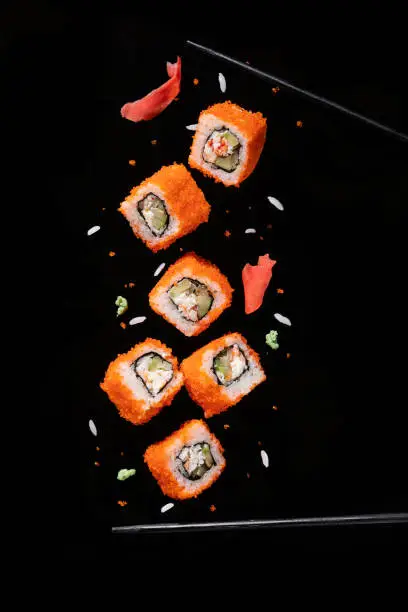 Sushi pieces between chopsticks, flying separated on black background.
