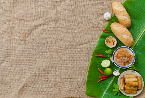 Vietnamese blank food background with Banh Mi, spring roll and shrimp dumpling on a green banana leaf and sedge fabric