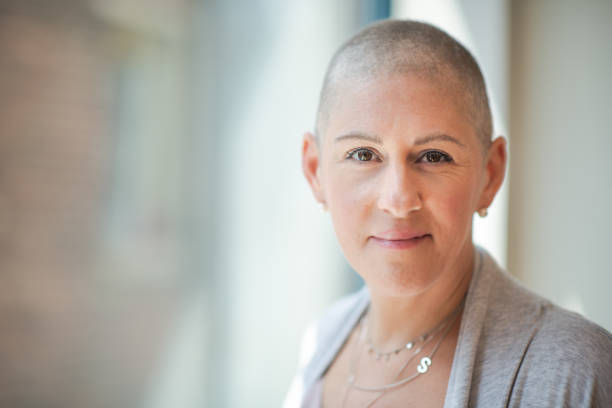 Portrait of a courageous woman with cancer Portrait of a courageous woman with cancer sitting near a window at a treatment center. The woman has a shaved head because chemotherapy treatment has caused hair loss. She is smiling softly while looking directly at the camera. She is filled with hope and gratitude. oncology photos stock pictures, royalty-free photos & images