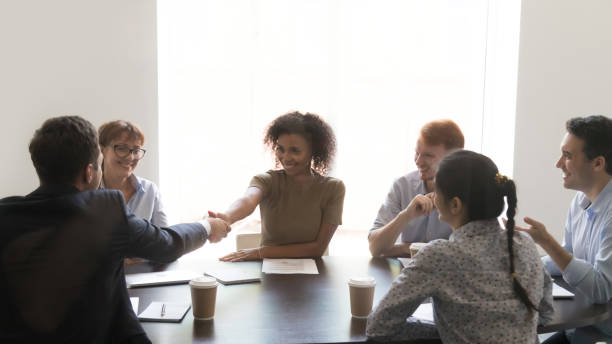 diversos socios comerciales reunidos en la sala de juntas distando la mano - exam business caucasian board room fotografías e imágenes de stock