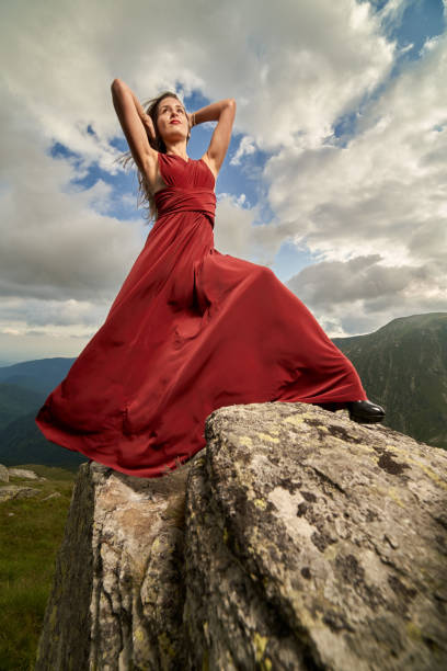 Beautiful female fashion model in red dress on mountain rocks