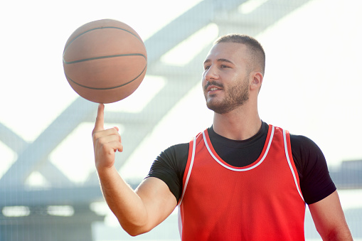 The basketball player is spinning basketball ball on finger, streetball, fun and skill concept.