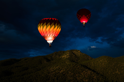 Two glowing hot air balloons in a night sky floating over a mountain