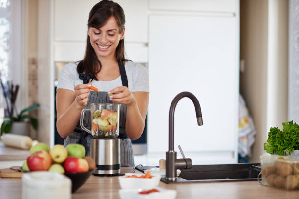 istock Woman putting vegetables and fruits in blender while standing in kitchen. 1167836021