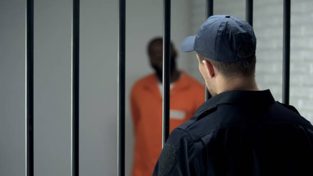 Warden looking at dangerous criminal standing in cell, life sentence, prison Warden looking at dangerous criminal standing in cell, life sentence, prison prison guard stock pictures, royalty-free photos & images